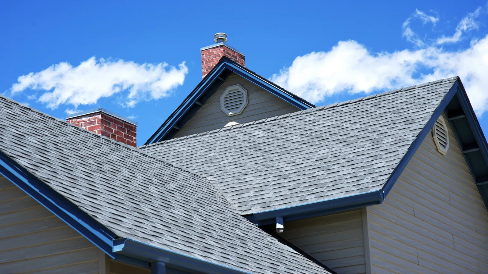 Brick chimneys and gray shingle rooflines against a bright blue sky