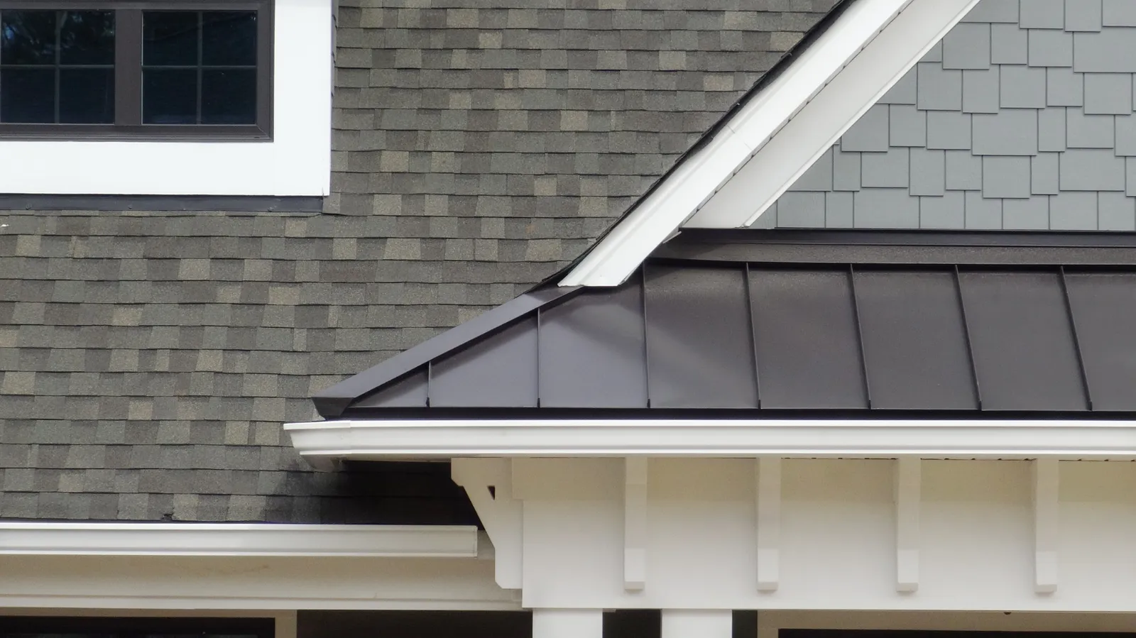 Gray shingle roof meeting a dark standing seam roof with white trim