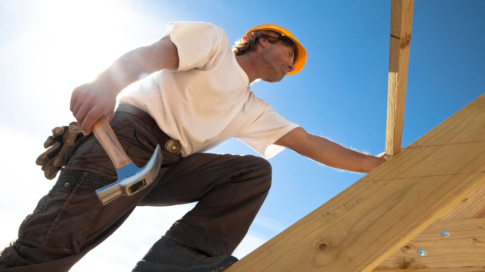 Hammer in hand a roofer climbs wooden roof framing