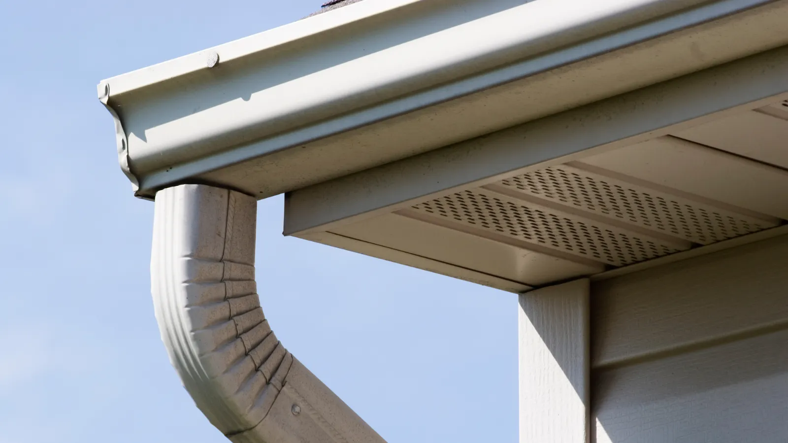At a corner with vented soffit a white gutter and downspout