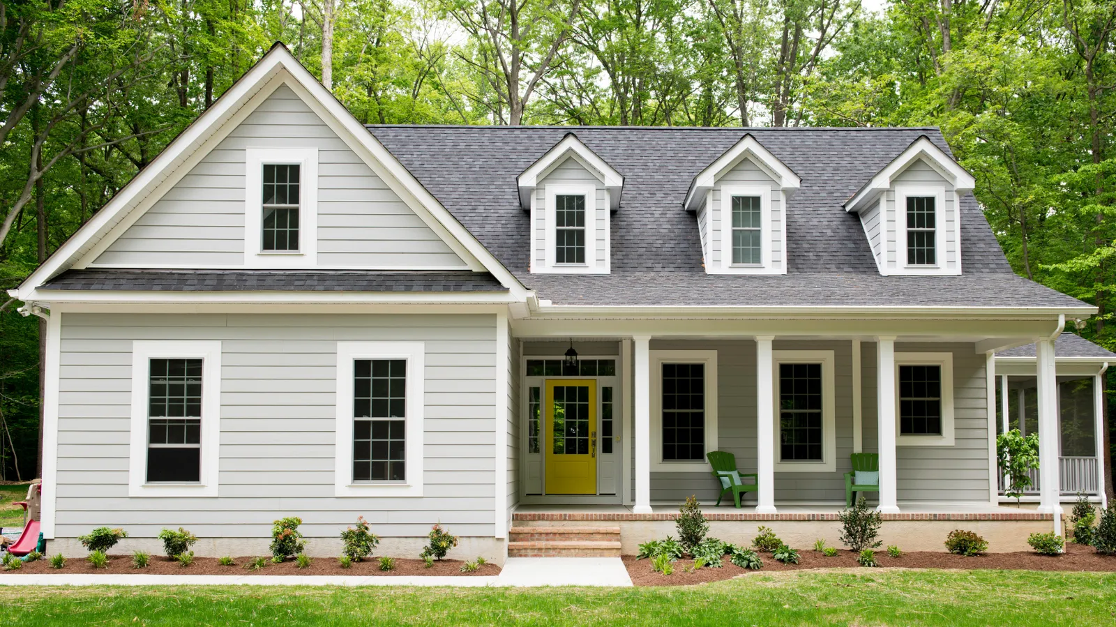 Gray house featuring a dark gray shingle roof with dormers and yellow front door