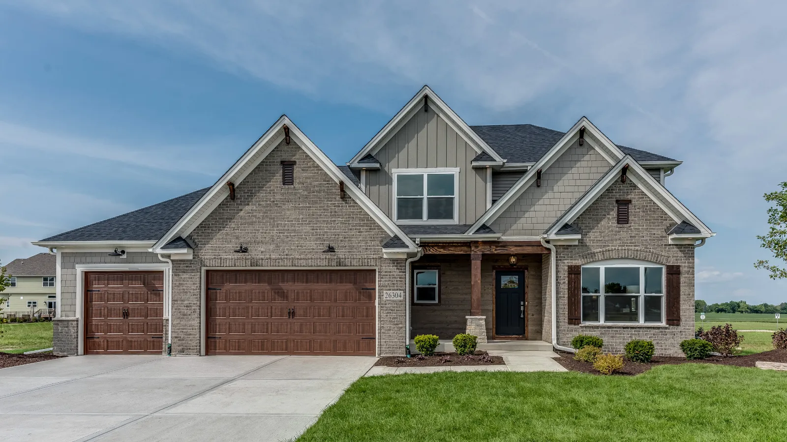 Gray brick craftsman home with wood garage doors and dark shingle roof