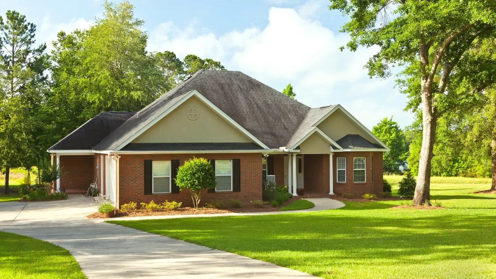 Mature trees shading a brick ranch home with gray shingle roof