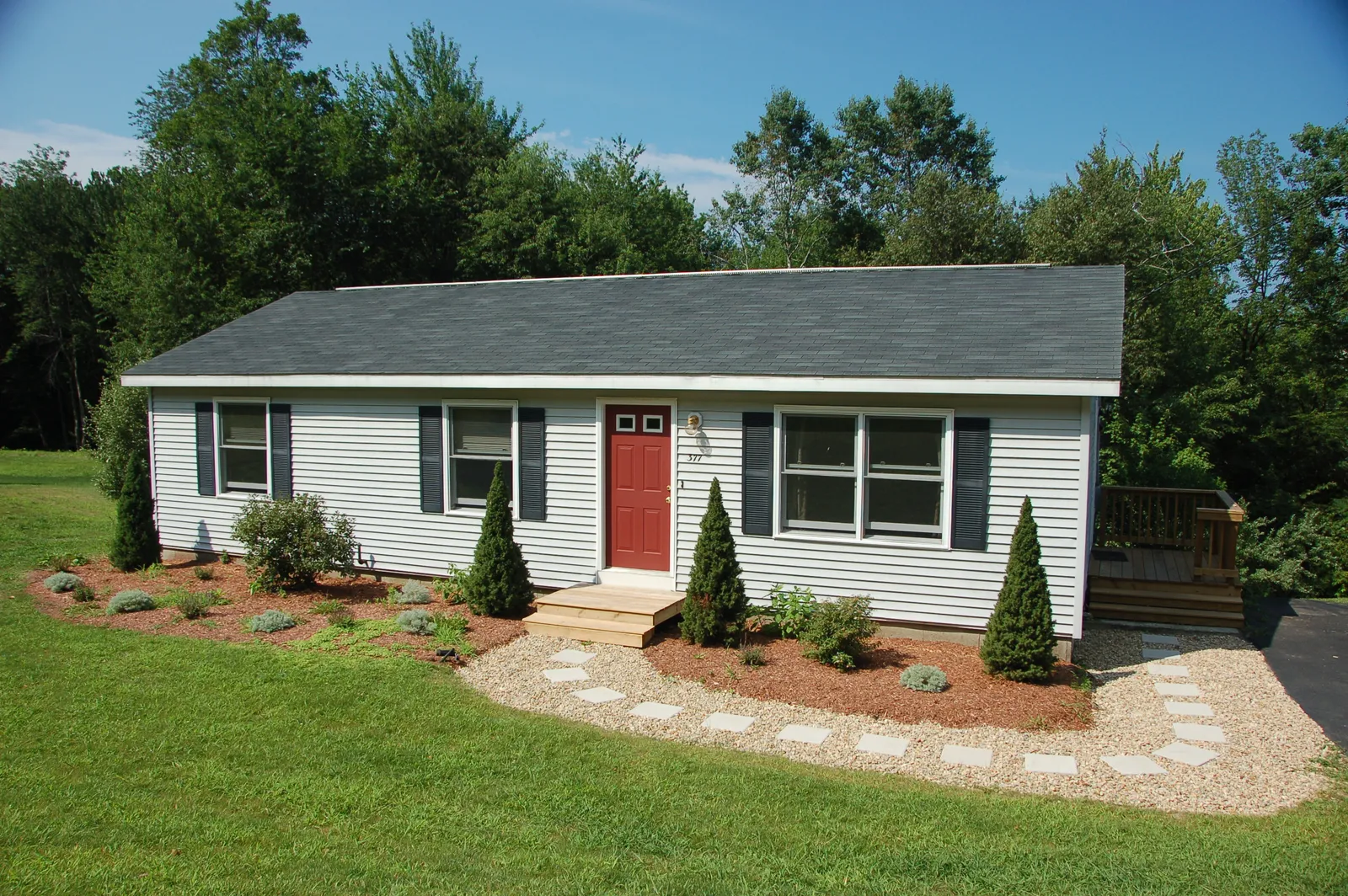 Red front door on a small ranch home under a dark shingle roof