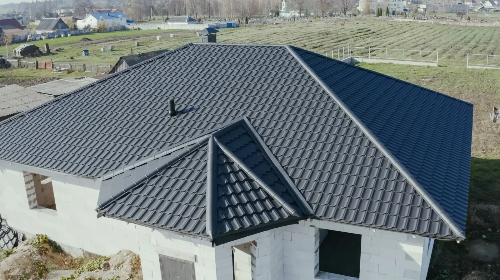 Dark metal tile hip roof on a block house with fields beyond